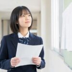 通知表を手に、成績4がつく基準を考える制服姿の中学生