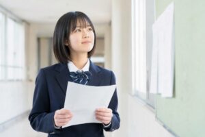 通知表を手に、成績4がつく基準を考える制服姿の中学生