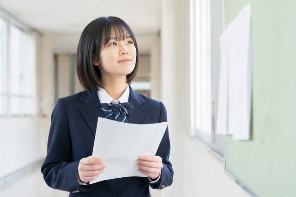 通知表を手に、成績4がつく基準を考える制服姿の中学生