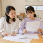 ダイニングで、点数が下がり続けるグラフの用紙を中学生の娘と母親が並んで見ている様子