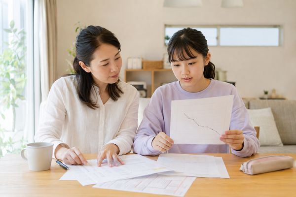 ダイニングで、点数が下がり続けるグラフの用紙を中学生の娘と母親が並んで見ている様子