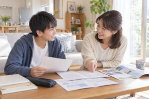 リビングのテーブルで、中学生の息子と母親が高校の学校案内や模試の成績表を広げ、笑顔で志望校について話し合っている様子