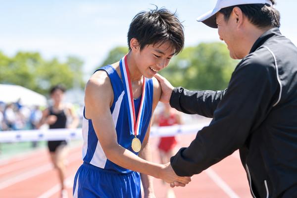 陸上大会でメダルを首にかけ、コーチと握手する中学生