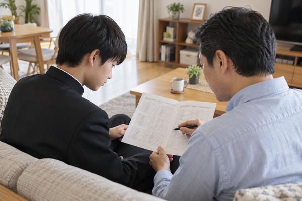 自宅のソファで、高校生の息子と父親が通知表を開いて確認している場面