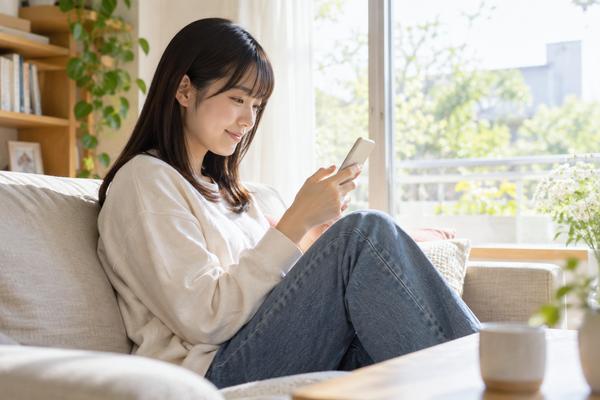 自宅のソファで、受験を終えた学生がスマートフォンのマイページを開いて成績を確認している場面