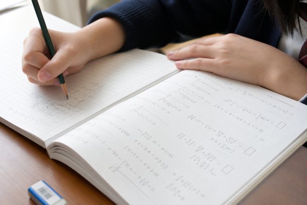 数学の参考書の例題を見ながら、方眼ノートに自分で式を書き進める高校生の手元