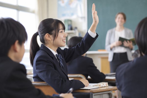 明るい教室で制服姿の中学生が英語の授業に手を挙げて発言している様子