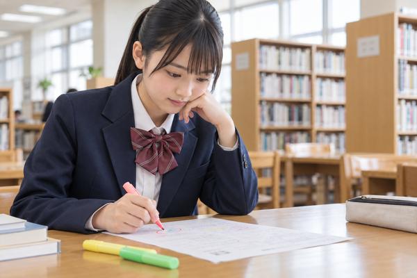図書室で返ってきた答案にマーカーで印を付ける制服の中学生