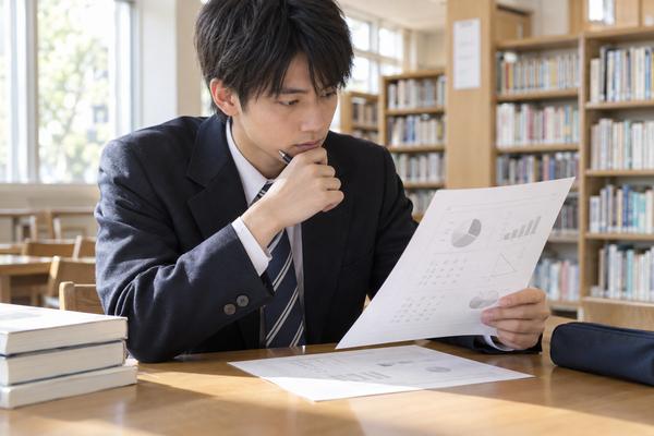 学校の図書室で、返却されたグラフ入りの模試成績表を制服の高校生が真剣に読んでいる様子