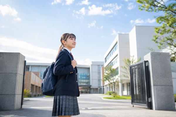 秋の青空の下、志望校の校門前で校舎を見上げている制服姿の中3の生徒