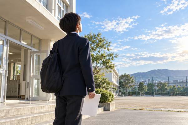 返却された答案を手に、校舎の前で立ち止まって考える中学生