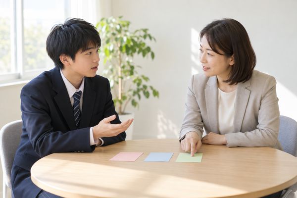 返却されたテストについて、色分けした3枚のカードを見ながら先生に質問する制服姿の男子高校生