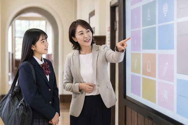 私立高校の明るい廊下でコース別の掲示を先生から説明してもらう制服の高校生