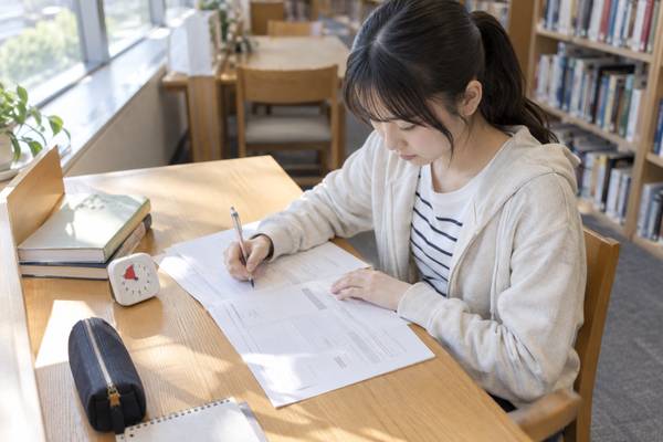図書館の自習席でタイマーを置き、時間を計って英語の過去問を解く高校生