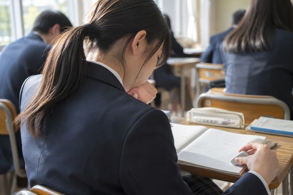 明るい教室で、制服の高校生が基本問題の途中で手が止まり考え込んでいる様子