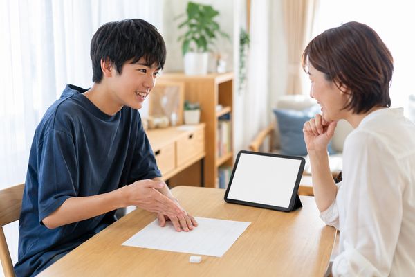 自宅のテーブルで中学生が答案を指しながら、正解の理由を保護者に説明している様子