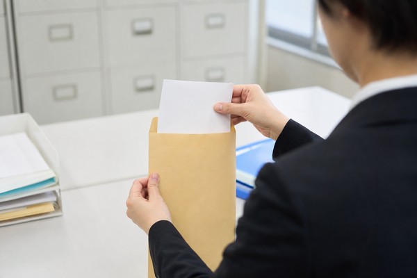 中学校の事務室で、調査書を無地の封筒に入れて封をする職員の手元