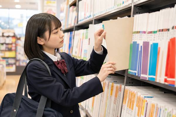 書店の学習参考書コーナーで、制服の女子高生が色分けされた見出しを見ながら一冊を選び出している様子