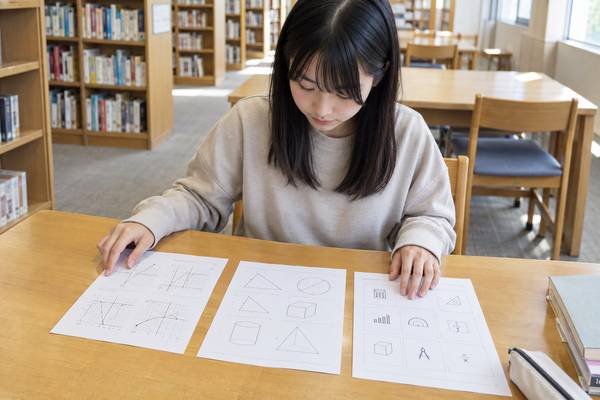 図書館の机で、中学生が3種類の数学プリントを並べて見比べている様子