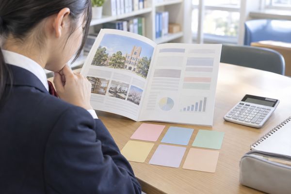 制服の高校生が大学案内と色分けカードで科目別の配点を確認している