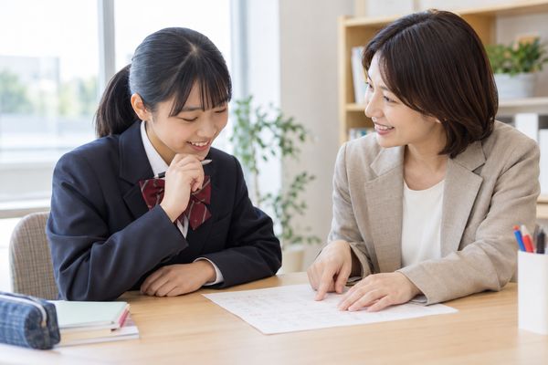 明るい部屋で制服の中学生と大人が、返却された答案を並べて一緒に見直している様子