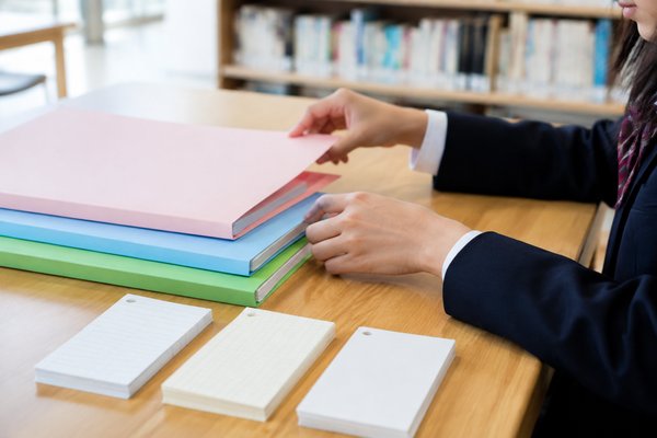 制服姿の中学生が図書室の机で3色のファイルとカードの束を種類ごとに分けている様子