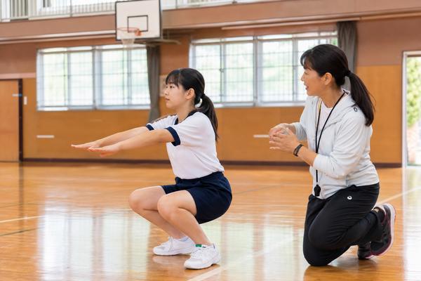 体育館で先生の助言を聞きながら動きを直していく体操服の中学生