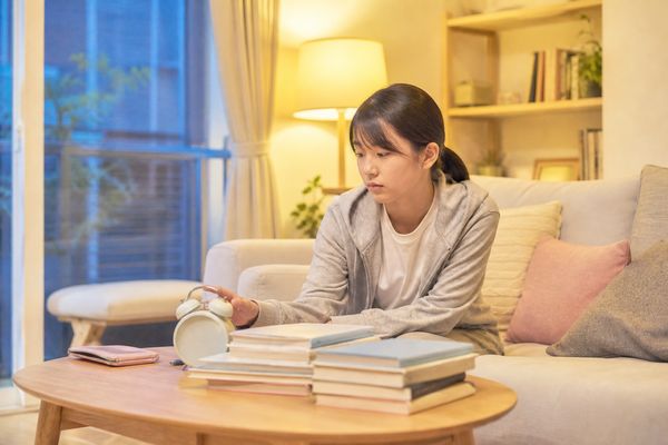 夜おそくに時計を見て、教材を閉じて休もうとする中3の女子生徒
