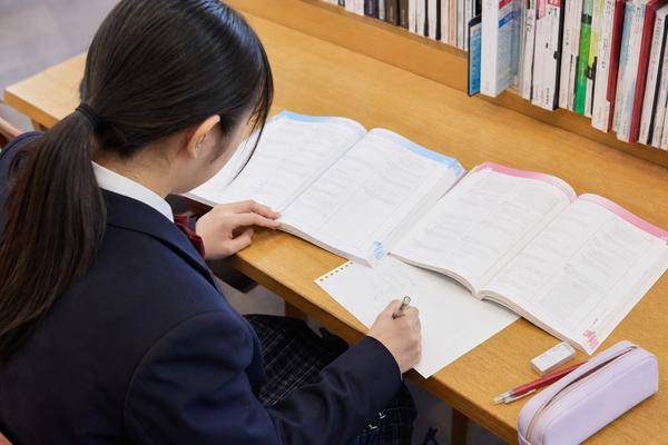 書店の閲覧席で2冊の参考書の例題を開いて解き比べ、紙に書き出している高校生