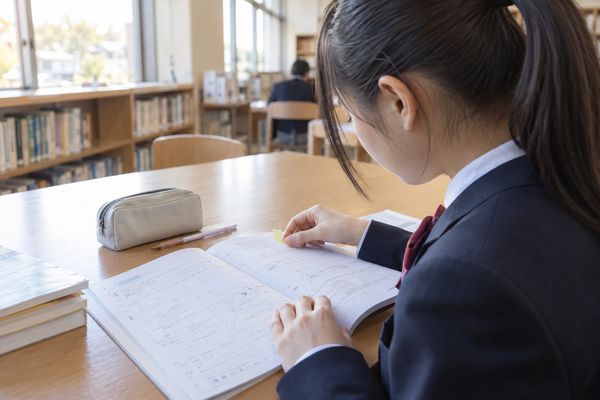 放課後の図書室で学校ワークに付箋を貼っていく制服姿の中学生