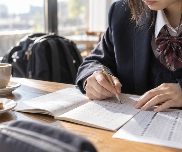制服姿の高校生が試験直後に、問題冊子へ控えた自分の解答と解答用紙を鉛筆で照らし合わせている手元