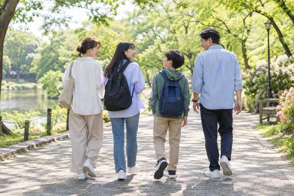 背の高さがそれぞれ違う両親ときょうだいの4人家族が、並木道を並んで歩いている後ろ姿