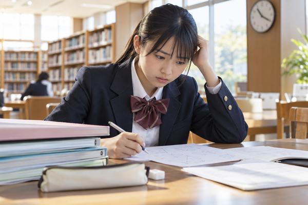 図書室で制服の高校生が模試の問題用紙を前に頭を抱え、解き方が浮かばず考え込んでいる様子