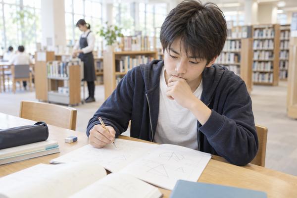 図書館の机で、私服の中学生が問題集を前に鉛筆を持ったまま手が止まり、どこでつまずいたのか考え込んでいる様子