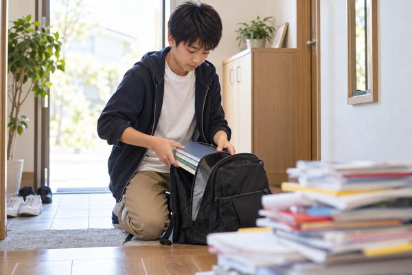 中1の男子生徒が学校ワーク・教科書・授業プリントだけを選んでカバンに入れ、雑多な本の山は手前に置いたままにしている様子