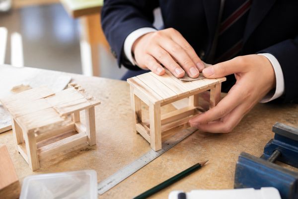 技術室で最初に作った試作と作り直した木製作品を見比べながら仕上げる中学生の手元