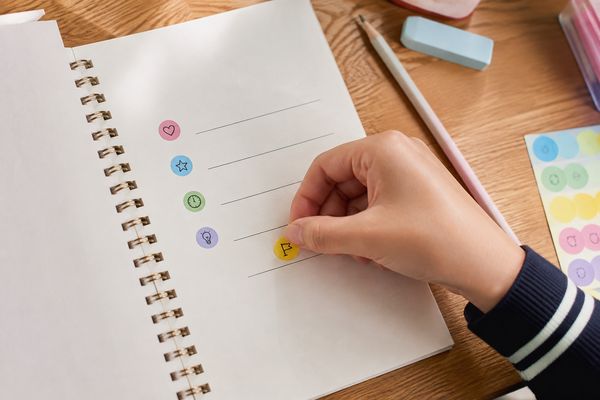 ノートの5本の空欄に教科ごとの色シールを貼り、成功記録を作ろうとしている中学生の手元