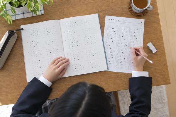 問題冊子へ控えた解答とマークシートの記入例を並べ、受験生が自己採点をしている手元