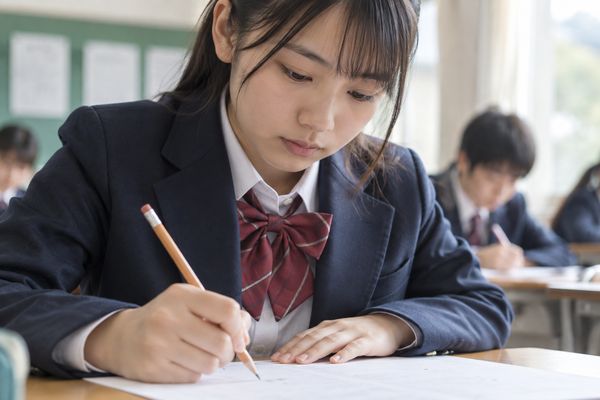 試験教室で制服姿の中学生が鉛筆を持ち、英作文の解答欄に書き始めている場面