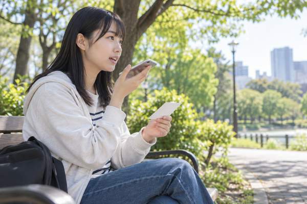 公園のベンチで単語カードを見ながらスマホに英文を声に出して練習する高校生