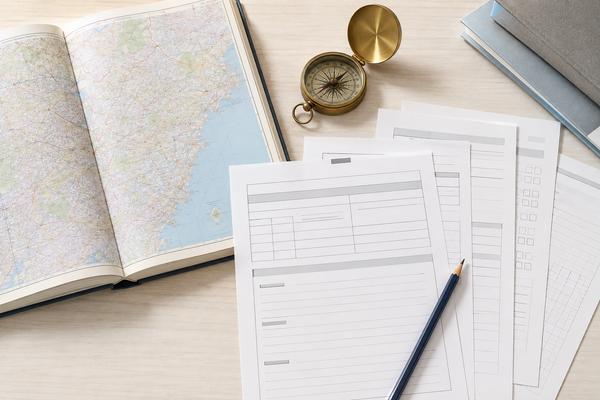 開いた地図帳と方位磁針のそばに入試案内らしい書類と鉛筆を並べ、地域ごとに計算方法が違うことを表した机の俯瞰