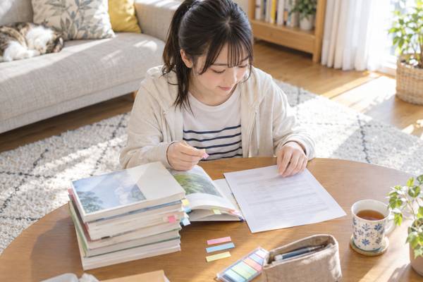 自宅のテーブルで、参考書と模試の案内プリントを広げて受験前の準備を進めている高校生