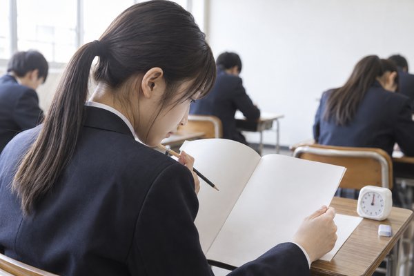 模試の会場で制服姿の高校生が机上の時計を横に置き、答案に途中式を書き進めている様子