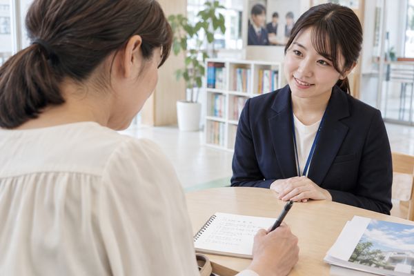 塾の面談席で、保護者が質問を書き出したノートにペンを添えながら、向かいの塾スタッフの説明を聞いている様子