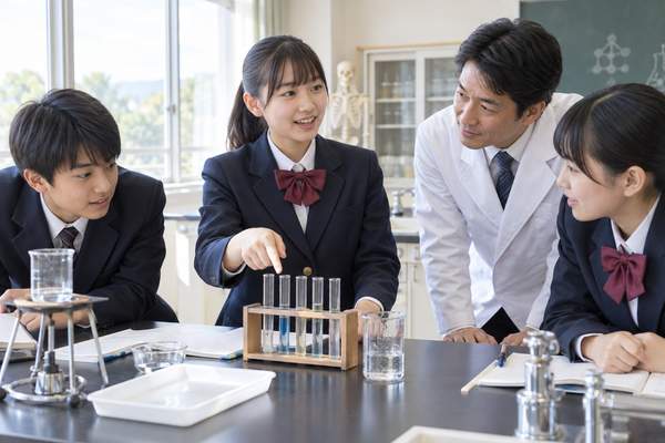 理科室で実験結果を先生と班の仲間に説明している制服姿の中学生