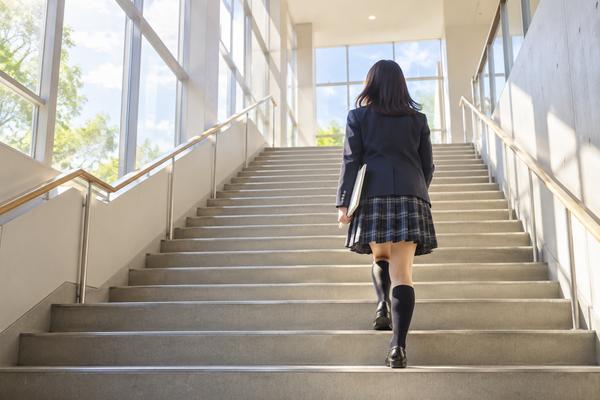 明るい校舎の階段を一段ずつ上っていく高校生の後ろ姿。単位を積み上げて卒業へ向かう様子