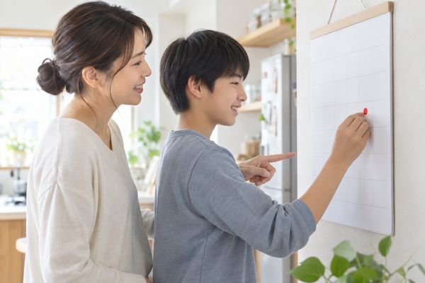 決めた宿題をやった日に、母親と中学生が壁のカレンダーへ印をつけている場面