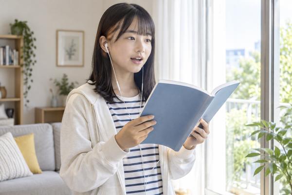 中1の女子生徒が窓辺でイヤホンをつけ、英語の教科書を開いて声に出して音読している様子