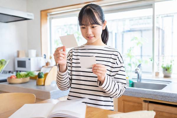 私服の中学生が明るいキッチンで参考書を伏せ、単語カードを使って自力で思い出せるか確認している様子