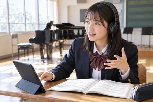 音楽室でヘッドホンをつけた中学生が、楽譜を開いて聴いた内容を声に出して説明している様子